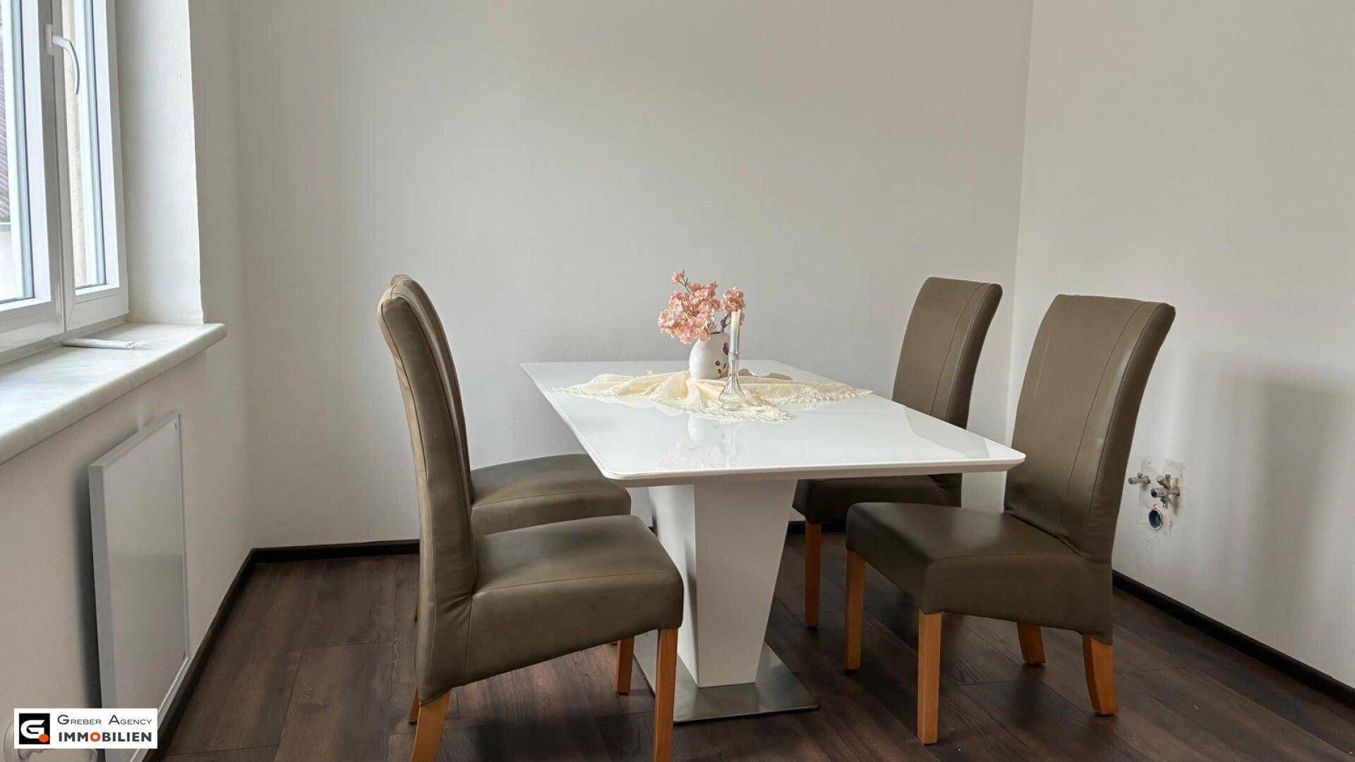 Heller Essbereich mit modernem weißen Tisch, braunen Stühlen und dunklem Laminatboden.