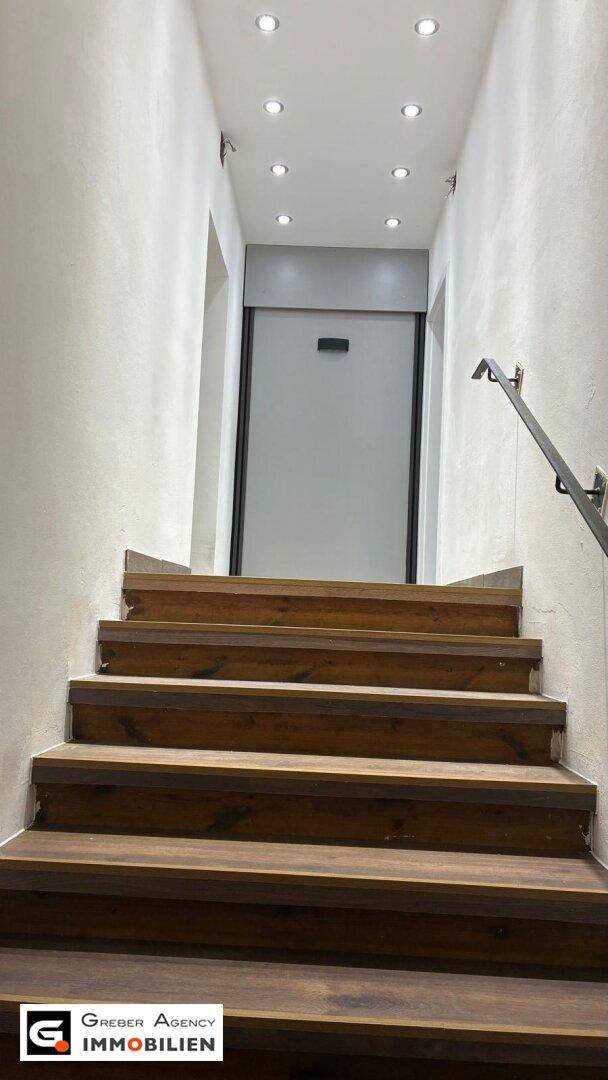 Holztreppe führt nach oben zu einem hellen Flur mit Einbaustrahlern in der Decke.