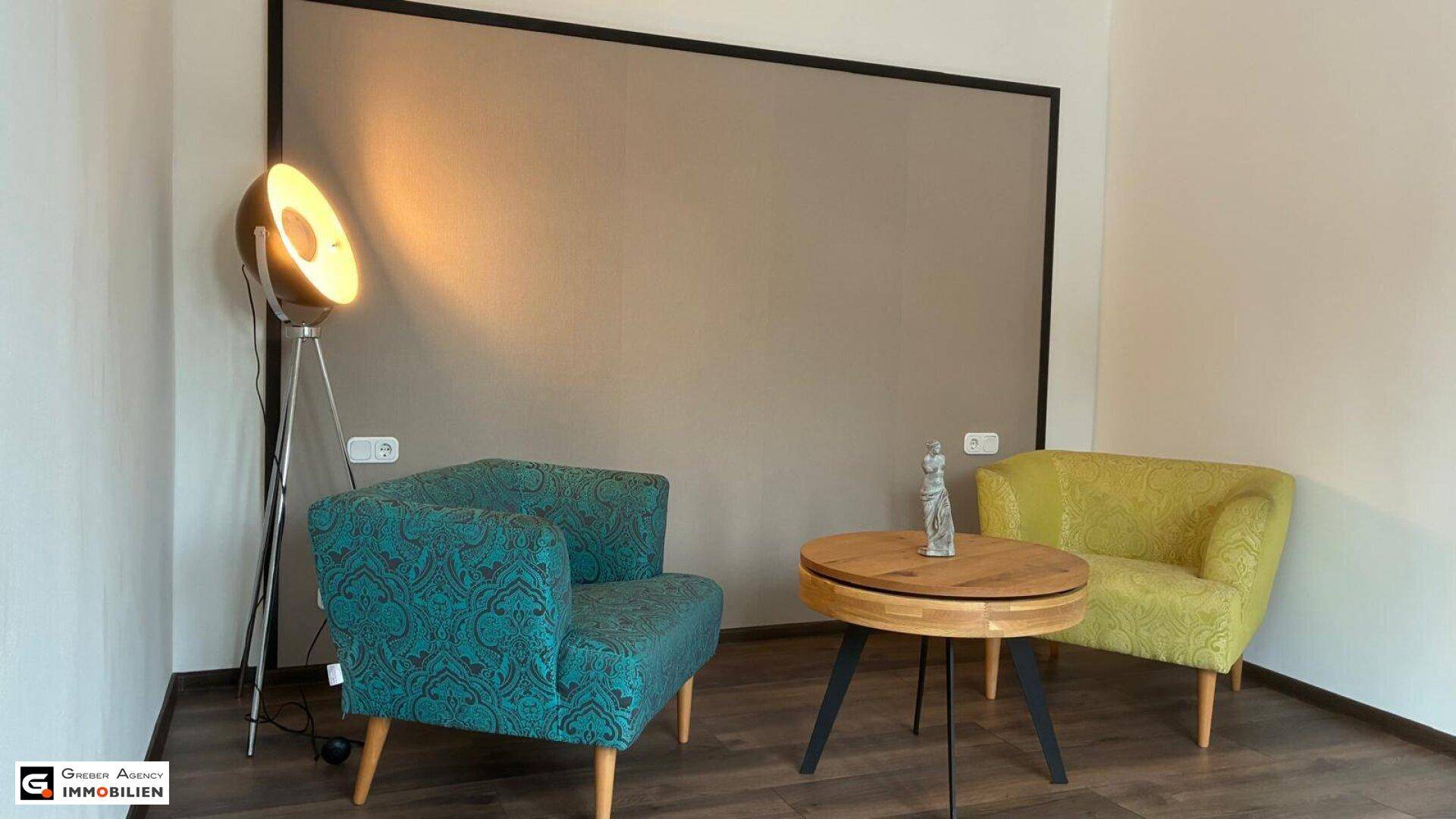 Gemütliche Sitzecke mit zwei farbigen Sesseln, einem runden Holztisch und Stehlampe.