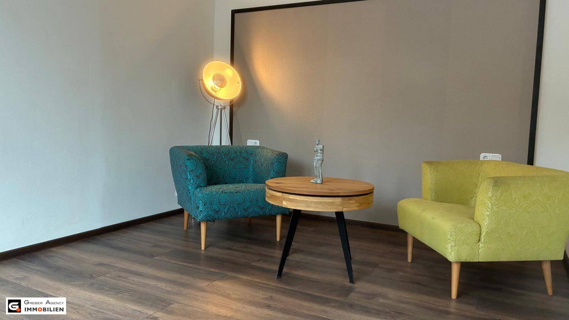 Wohnbereich mit modernen Sesseln in Türkis und Gelb, einem Couchtisch und Stehlampe.