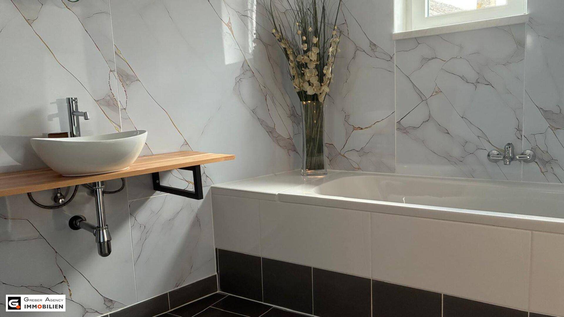 Modernes Badezimmer mit Badewanne, Aufsatzwaschbecken auf Holzplatte und Marmorfliesen.