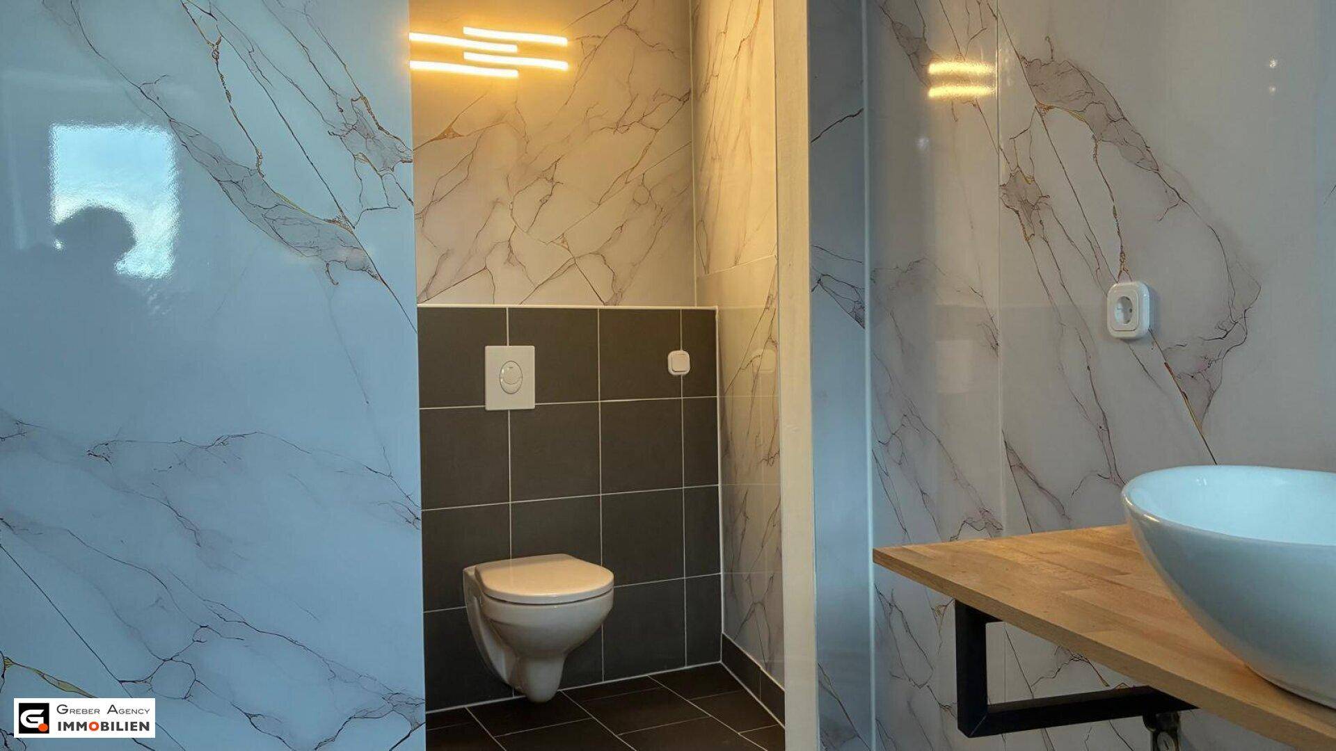 Badezimmer mit Wand-WC, Aufsatzwaschbecken und eleganten Fliesen in Marmoroptik.
