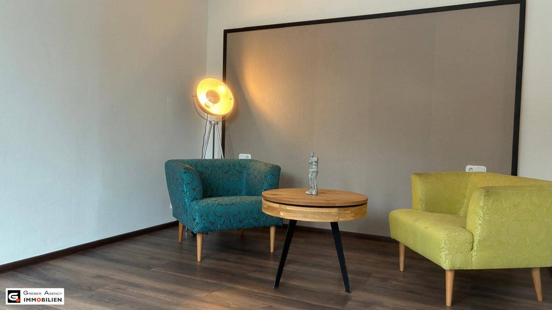 Helle Sitzecke mit farbigen Sesseln, einem runden Holztisch und einer modernen Stehlampe.