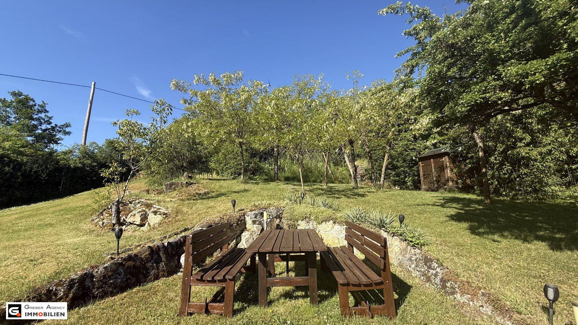 Gemütlicher Sitzbereich im Garten mit Holztisch und Bänken, umgeben von viel Grün.