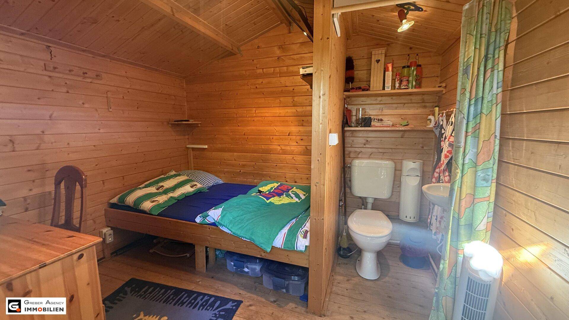 Rustikales Schlafzimmer mit Holzwänden und integriertem WC-Bereich, einfach eingerichtet.