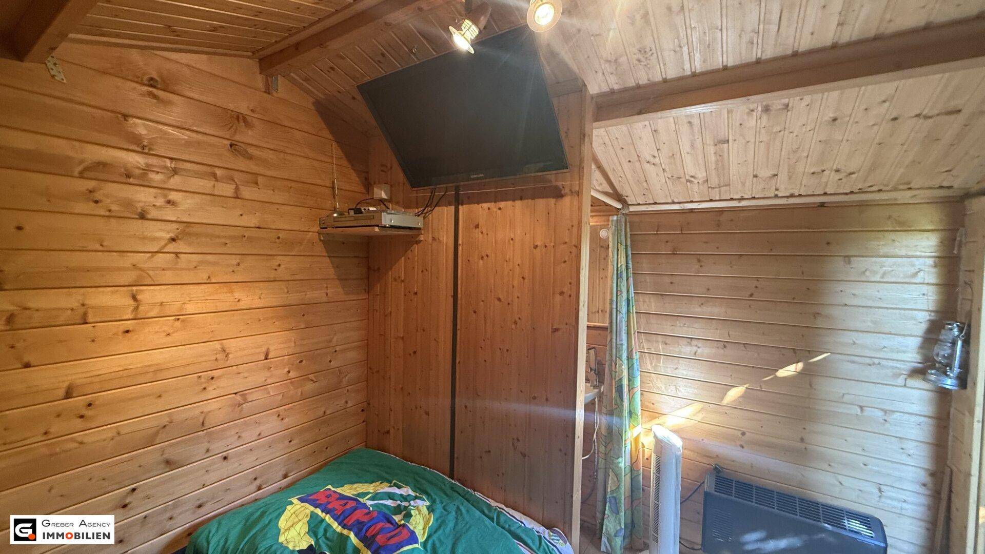 Gemütliches Schlafzimmer mit Holzwänden und -decke, ausgestattet mit einem Fernseher.