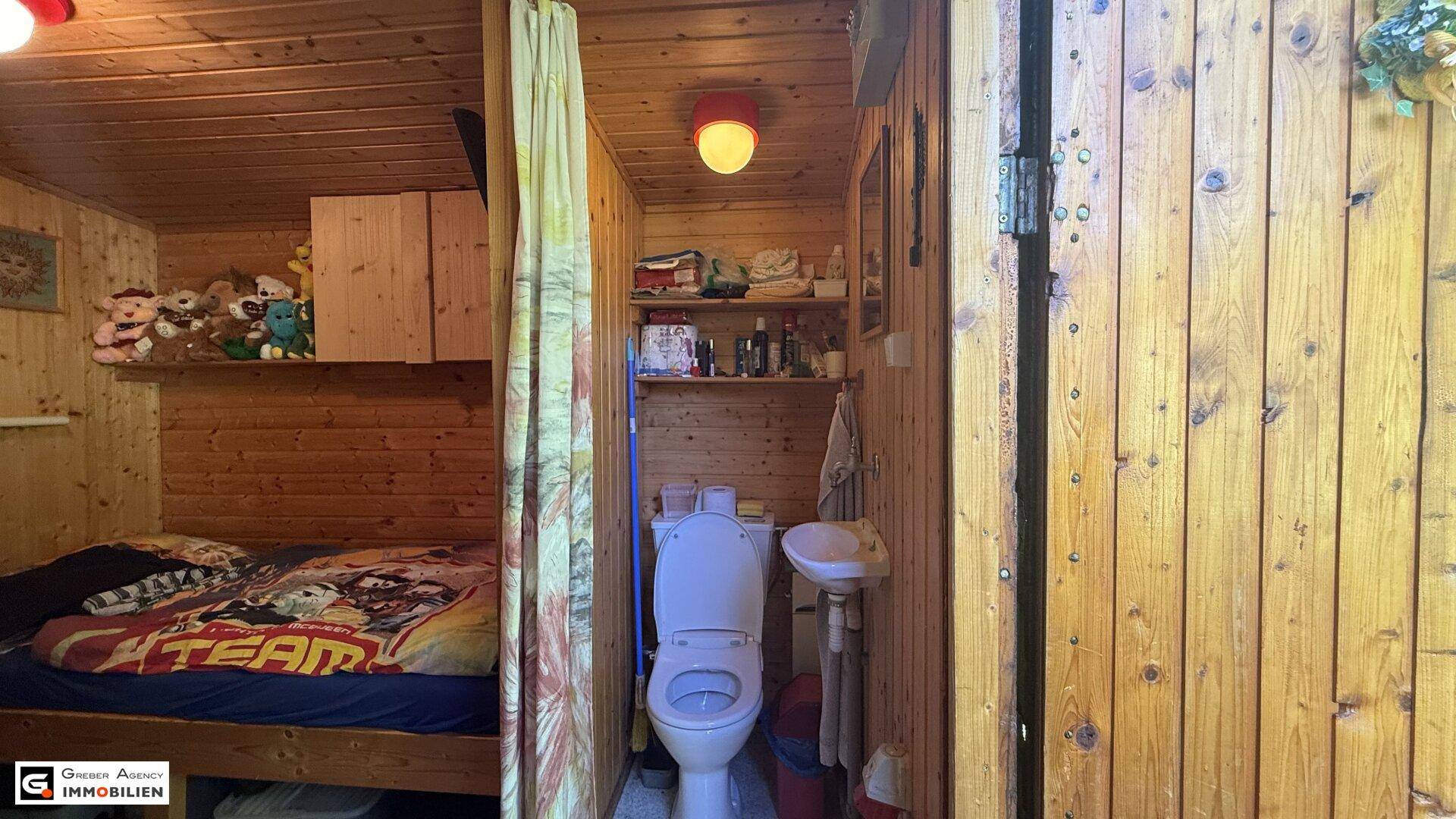 Einfaches Schlafzimmer mit Holzwänden und einem abgetrennten Bereich mit WC und Waschbecken.