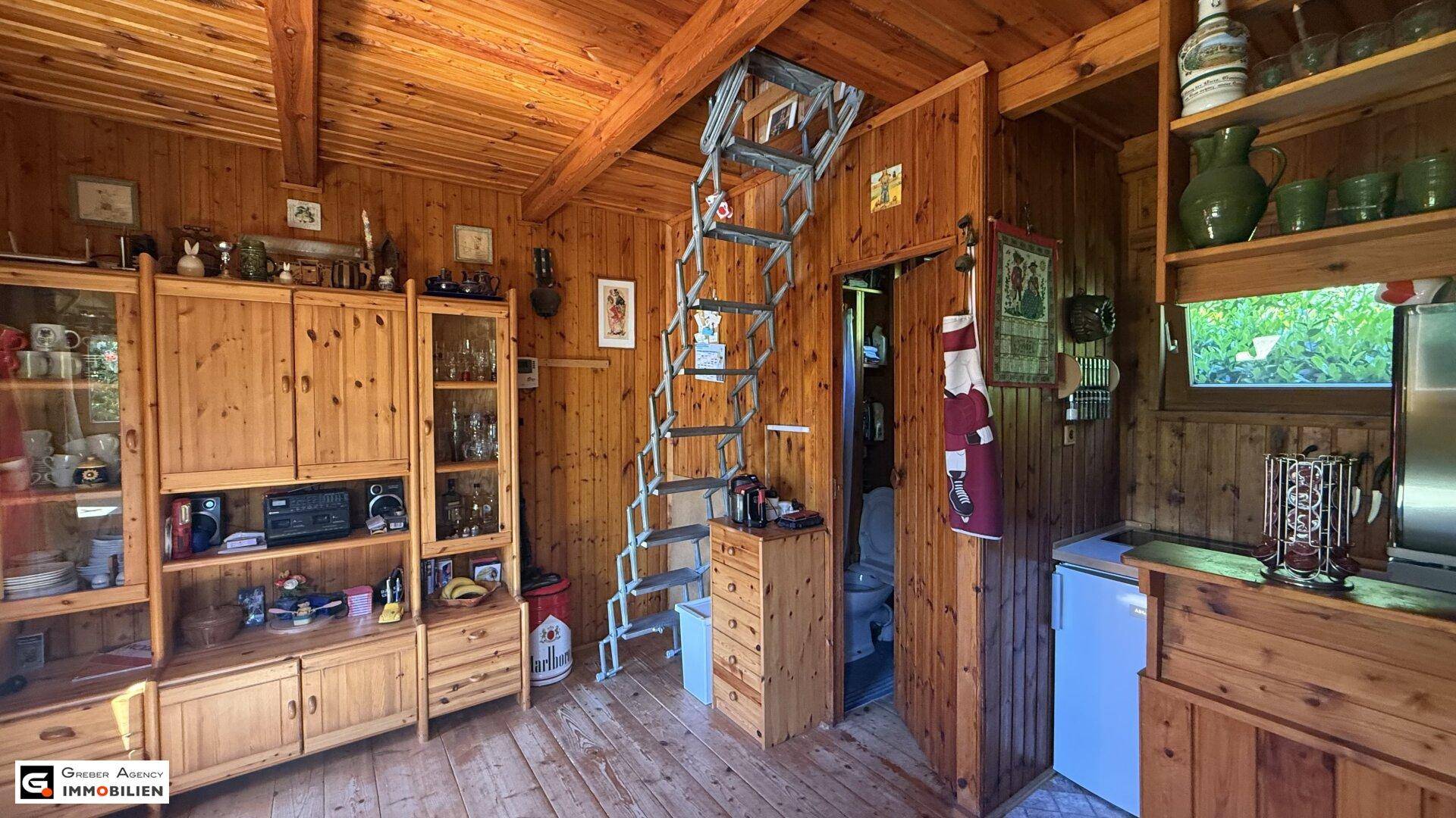 Rustikaler Wohnbereich mit Holzeinrichtung, kleiner Küchenzeile und ausziehbarer Treppe zum Dachboden.
