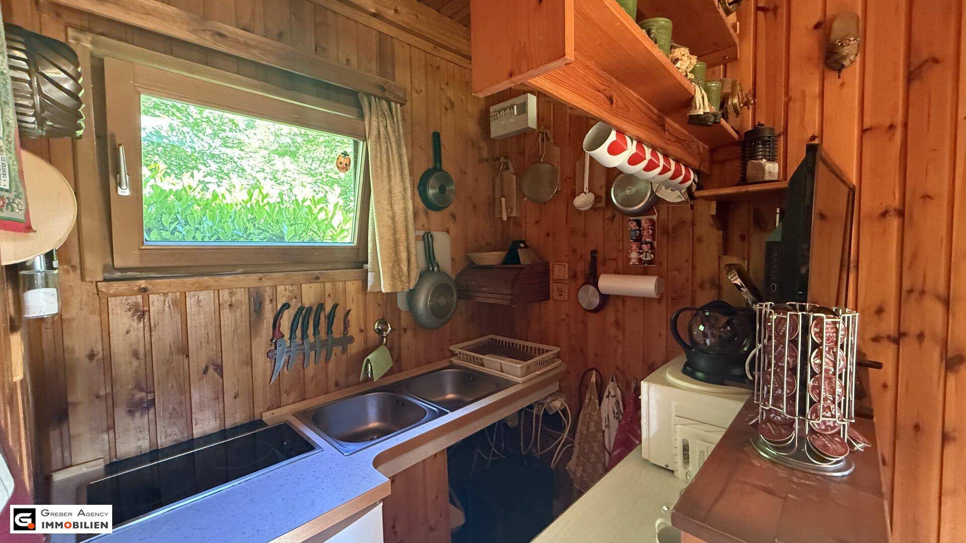 Kleine, funktionale Küche mit Holzwänden, Doppelspüle und Blick ins Grüne durch das Fenster.