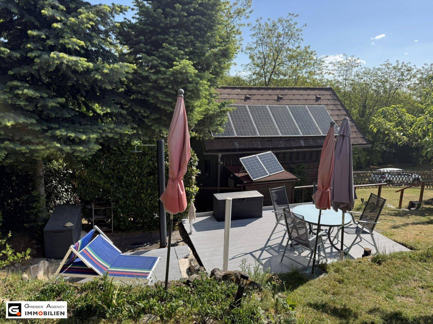 Sonnige Terrasse mit Liegestühlen und Gartenmöbeln, ergänzt durch Solarpaneele auf dem Dach.