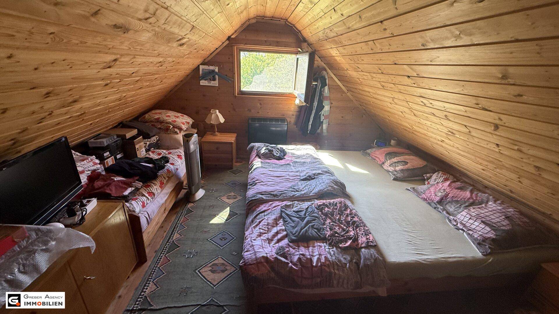 Gemütliches Schlafzimmer im Dachgeschoss mit schrägen Holzwänden und Dachfenster.