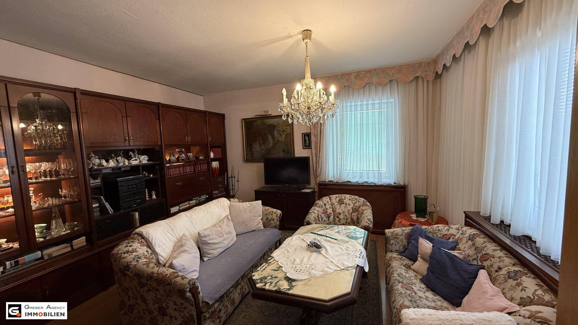Klassisches Wohnzimmer mit bequemen Sofas, Kronleuchter und großem Fenster mit Vorhängen für natürliches Licht.