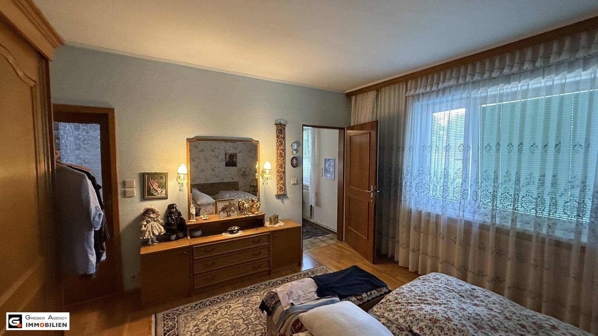Schlafzimmer mit Doppelbett, Kommode mit Spiegel und Fenster für natürliches Licht und Ausblick.