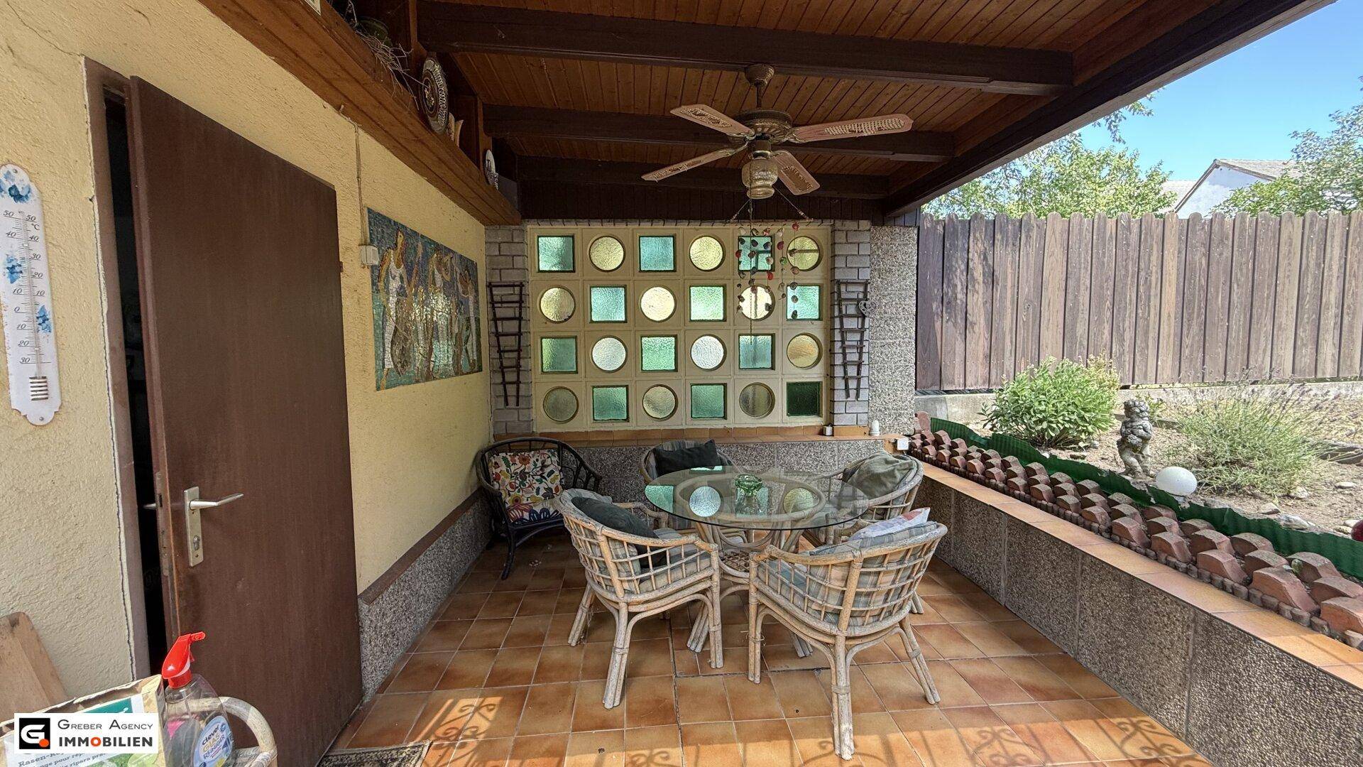 Überdachte Terrasse mit Sitzgelegenheiten, Deckenventilator und dekorativen Wandelementen für Entspannung.