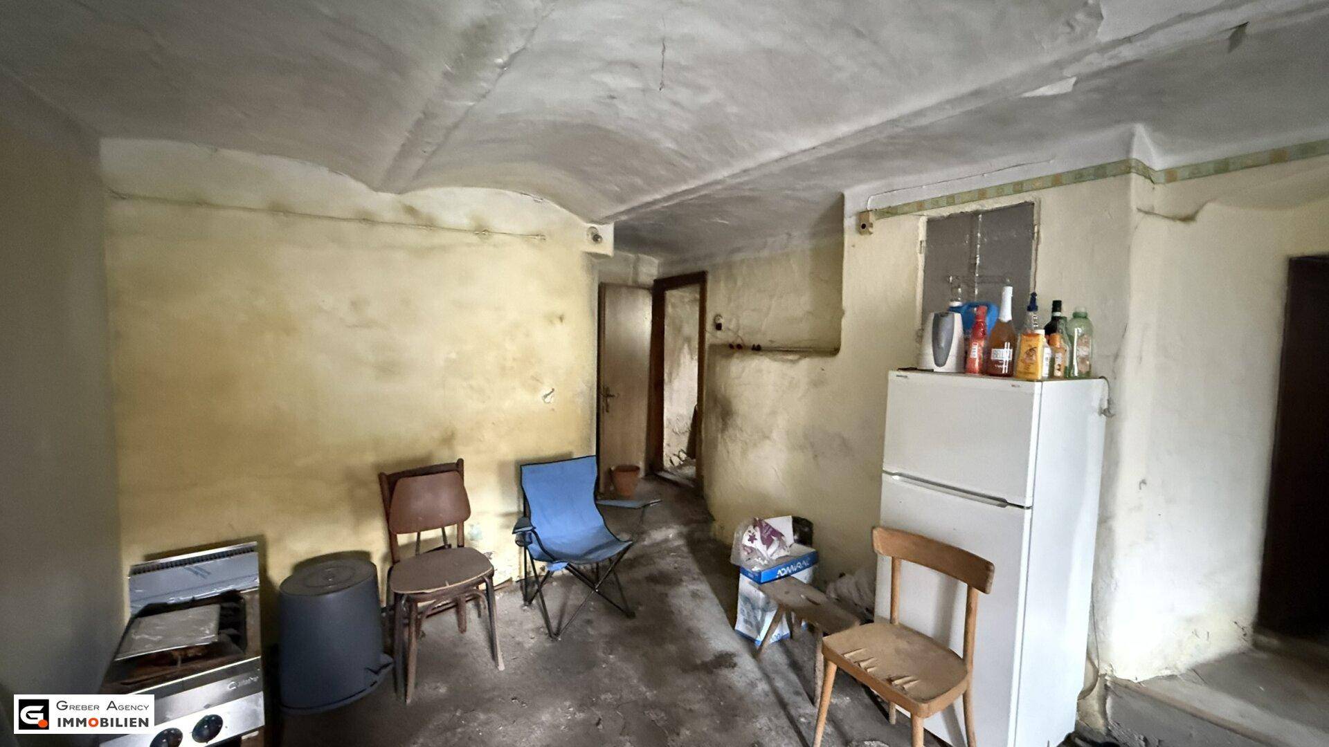 Kellerraum mit gewölbter Decke, alten Wänden, einem Kühlschrank und verschiedenen Möbelstücken.