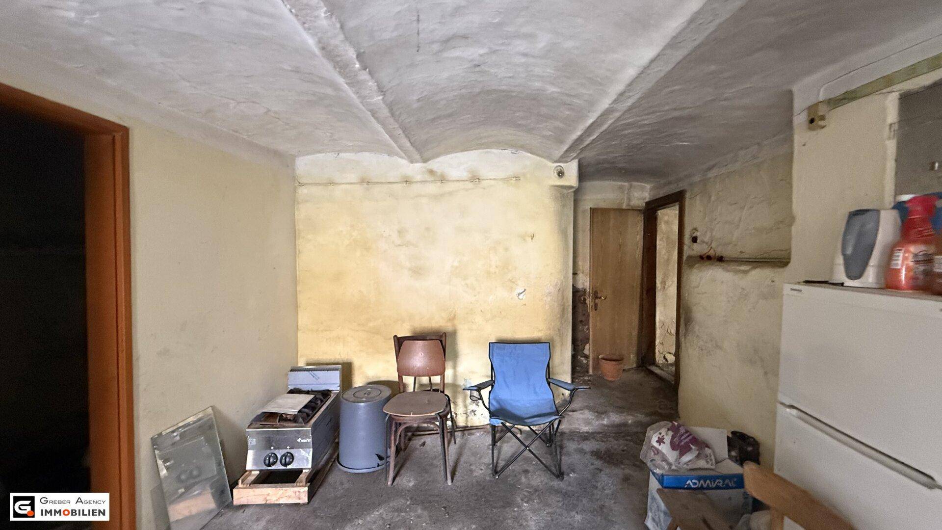 Geräumiger Kellerraum mit gewölbter Decke, einem Kühlschrank und einfachen Möbeln.