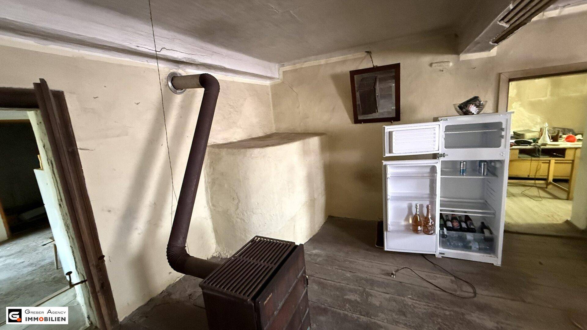 Einfacher Raum mit Holzboden, einem Holzofen, Kühlschrank und einem kleinen Spiegel.