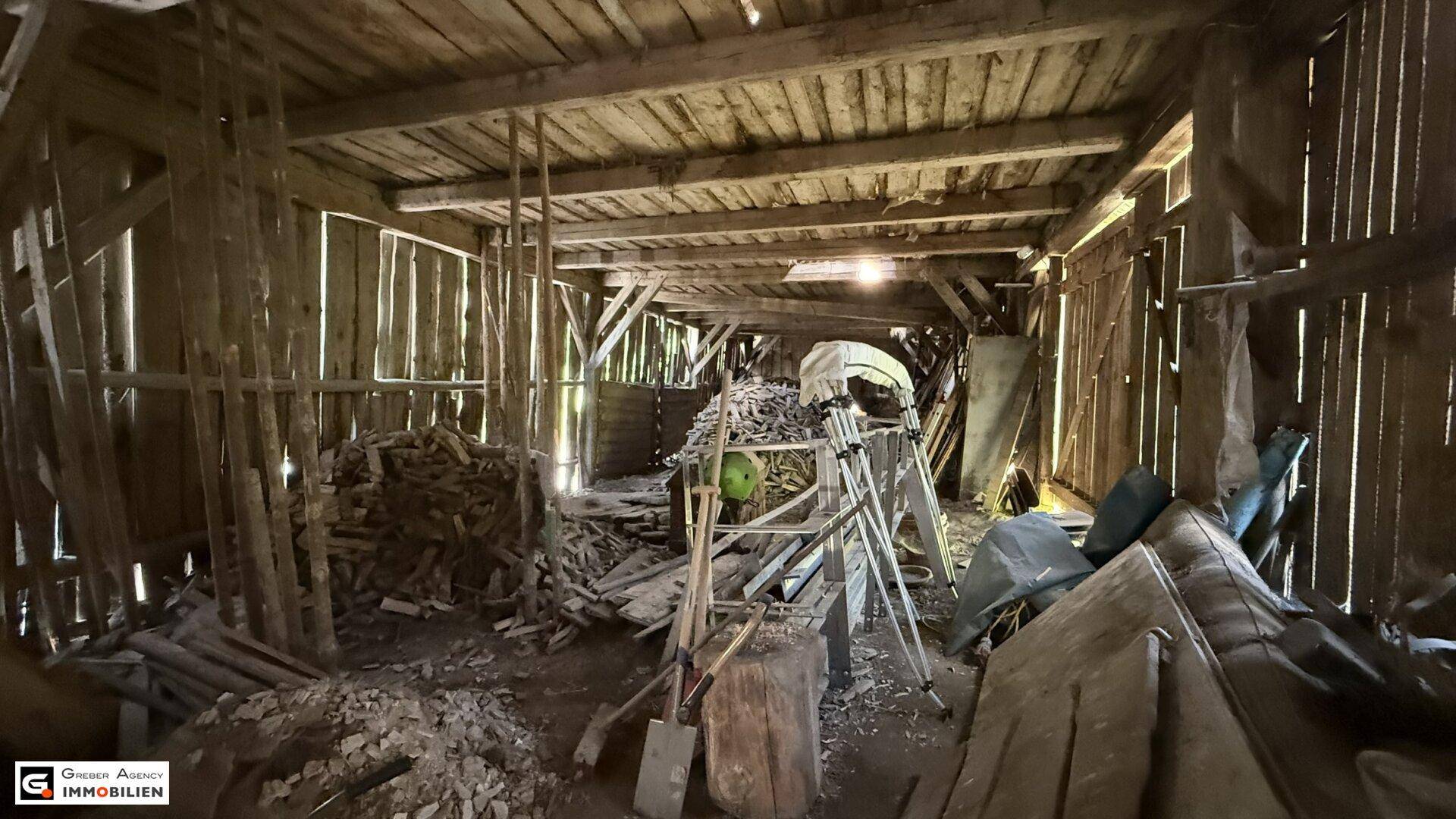 Großer Scheunenraum mit Holzbalken, gefüllt mit Holzscheiten und verschiedenen Materialien.