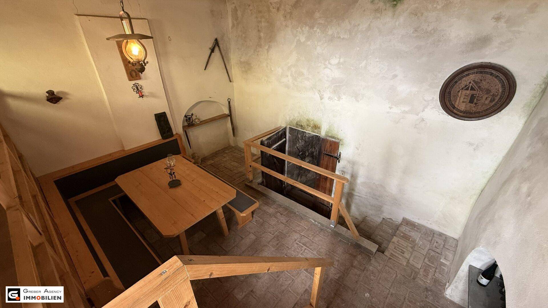 Rustikaler Essbereich mit Holzbänken und Tisch, daneben ein Abgang in einen Keller oder tieferen Bereich.