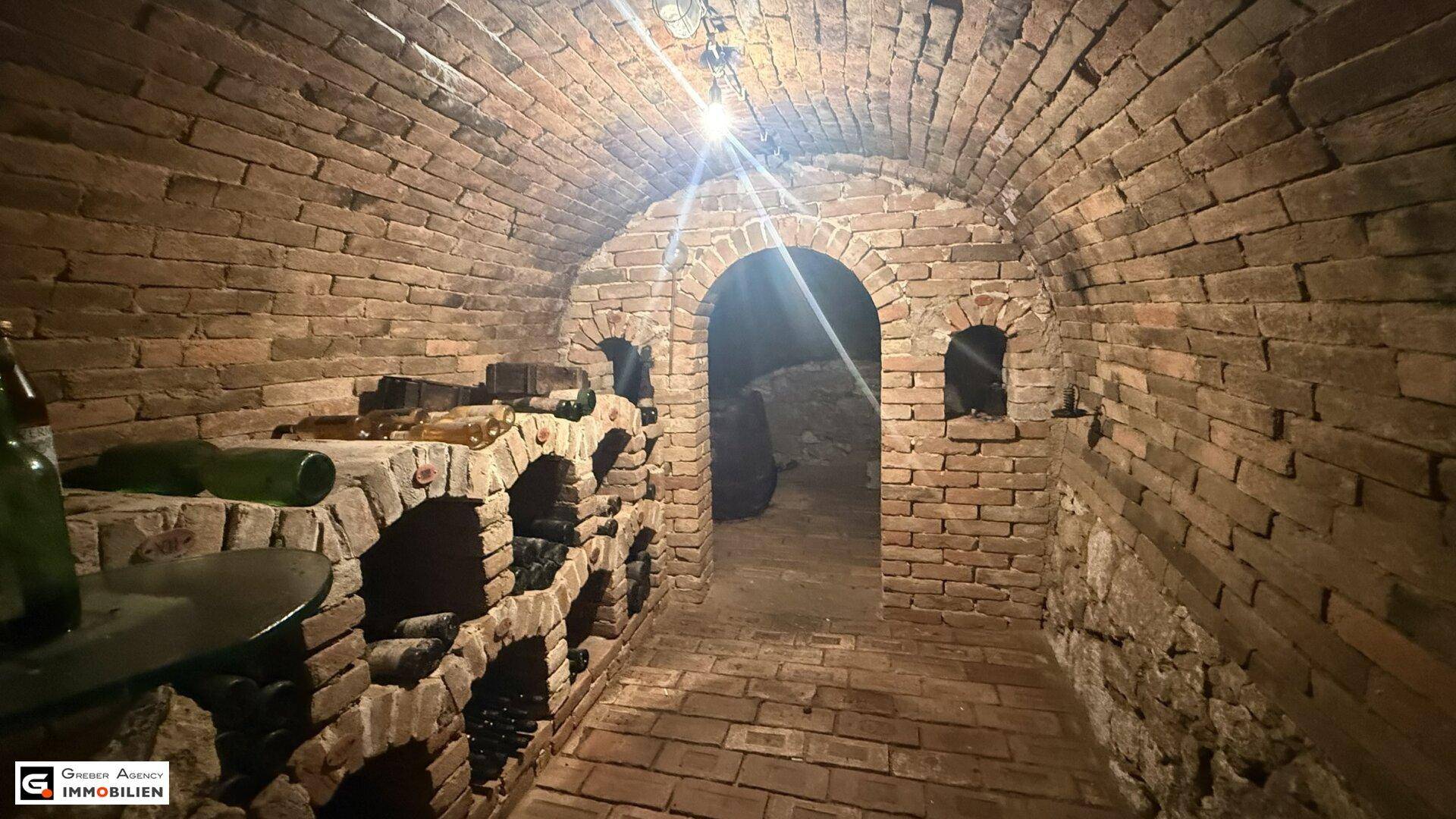 Historischer Weinkeller mit Ziegelgewölbe und integrierten Regalen für Weinflaschen, gut beleuchtet.