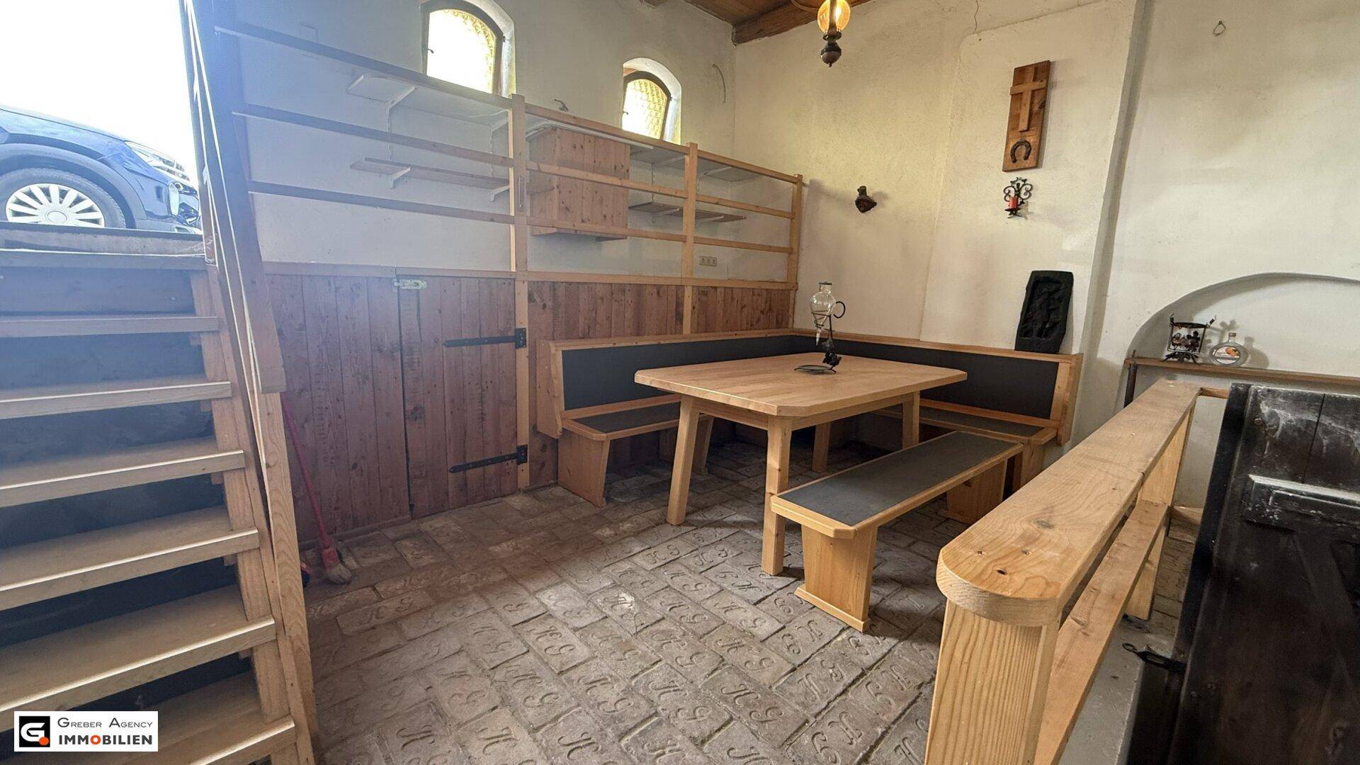 Gemütlicher Essbereich mit Holztisch und Bänken, daneben eine Holztreppe und offene Regale.