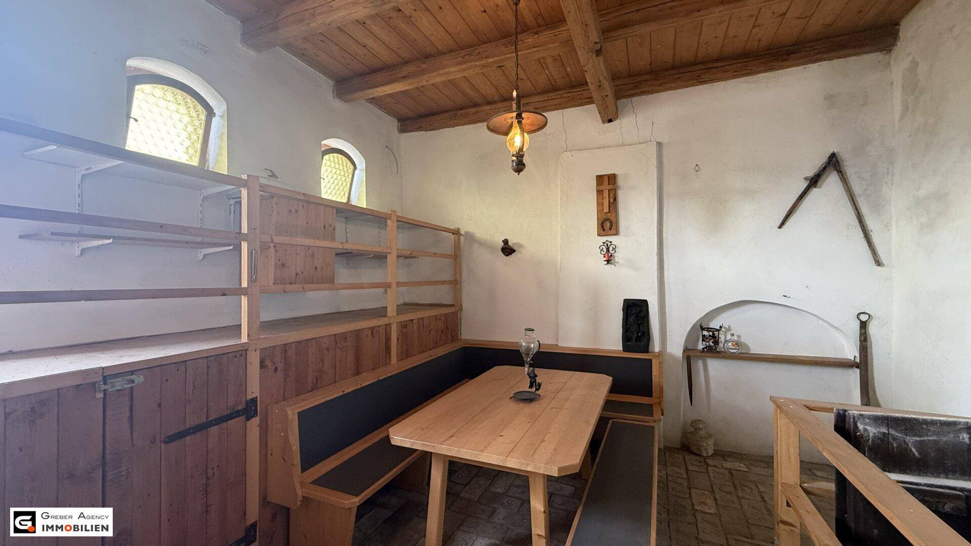 Rustikaler Essbereich mit Holztisch, Bänken und sichtbaren Deckenbalken, beleuchtet durch eine Hängelampe.