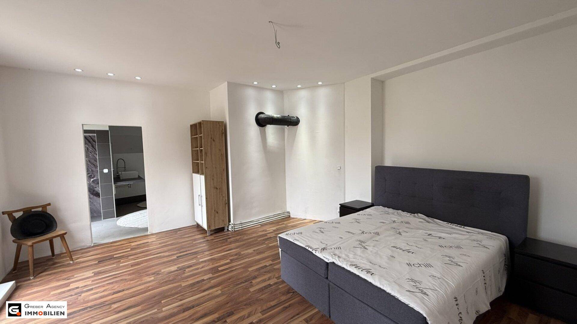 Geräumiges Schlafzimmer mit Holzboden, Doppelbett und Zugang zu einem weiteren Bad.