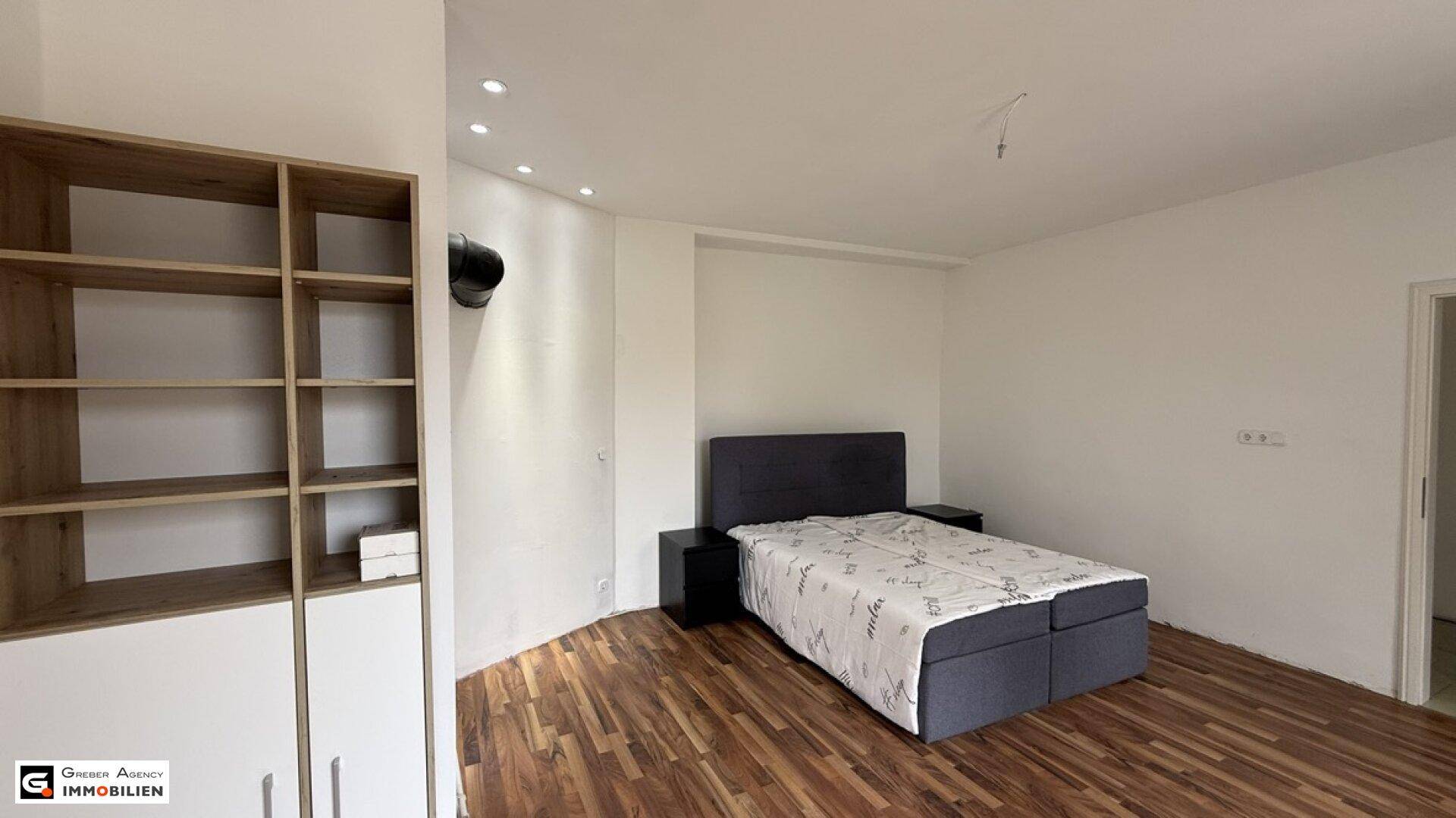 Helles Schlafzimmer mit Holzboden, Einbauregal und modernem Doppelbett.
