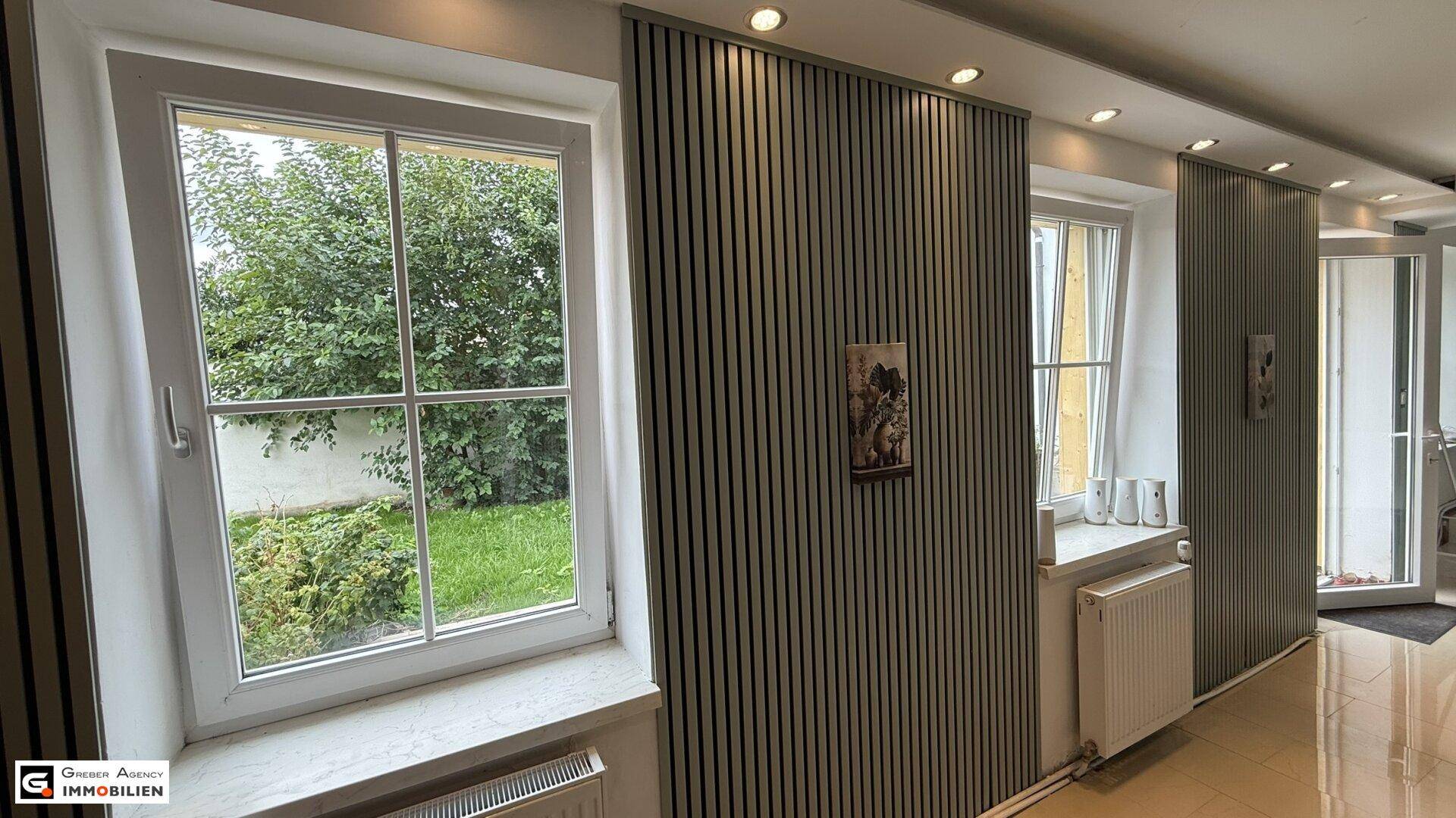 Heller Flur mit großen Fenstern, Blick in den Garten und stilvollen Wandverkleidungen.