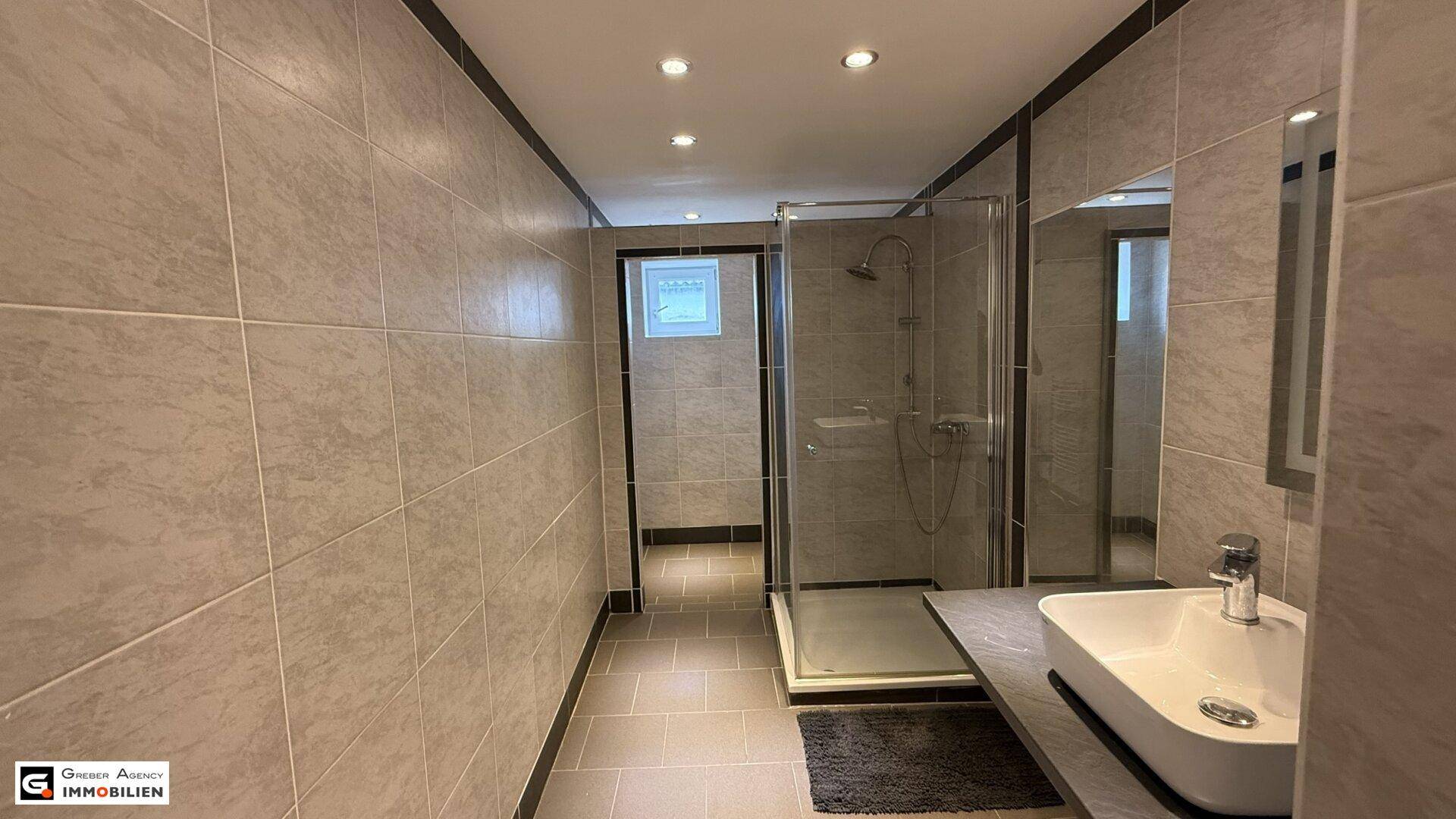 Modernes Badezimmer mit begehbarer Dusche, Waschbecken und hellen Fliesen.