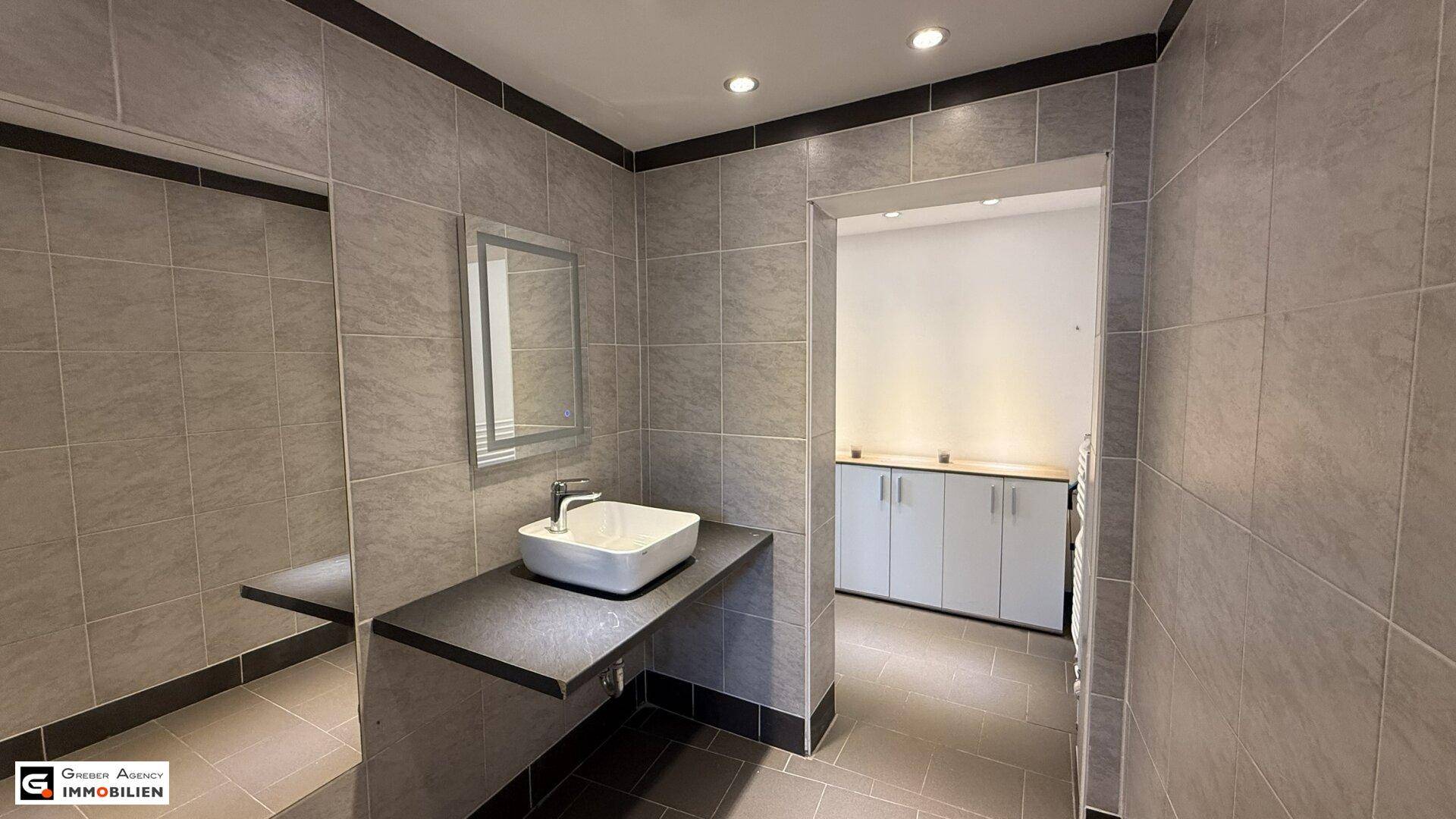 Helles Badezimmer mit modernem Waschbecken, Spiegel und angrenzendem Abstellraum.