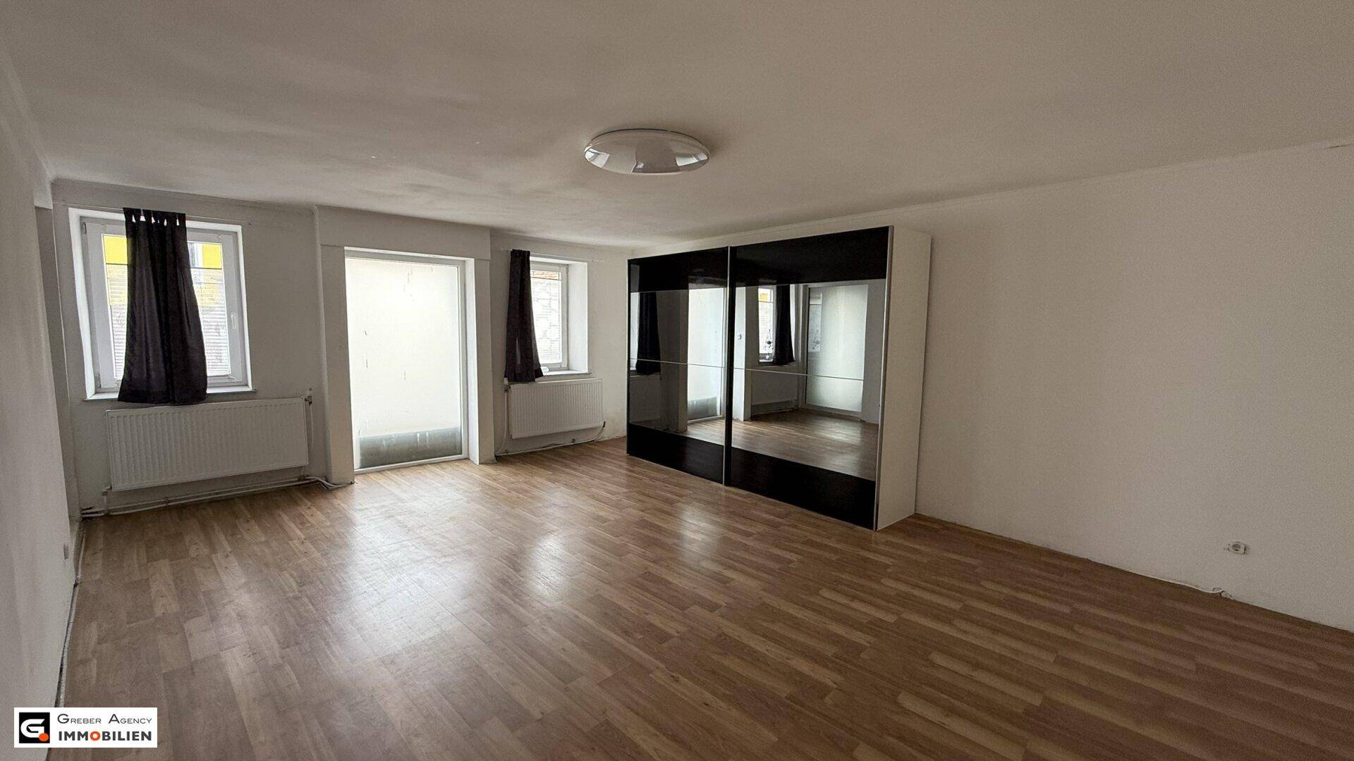 Geräumiges Schlafzimmer mit Holzboden, Spiegelschränken und Zugang zum Balkon.