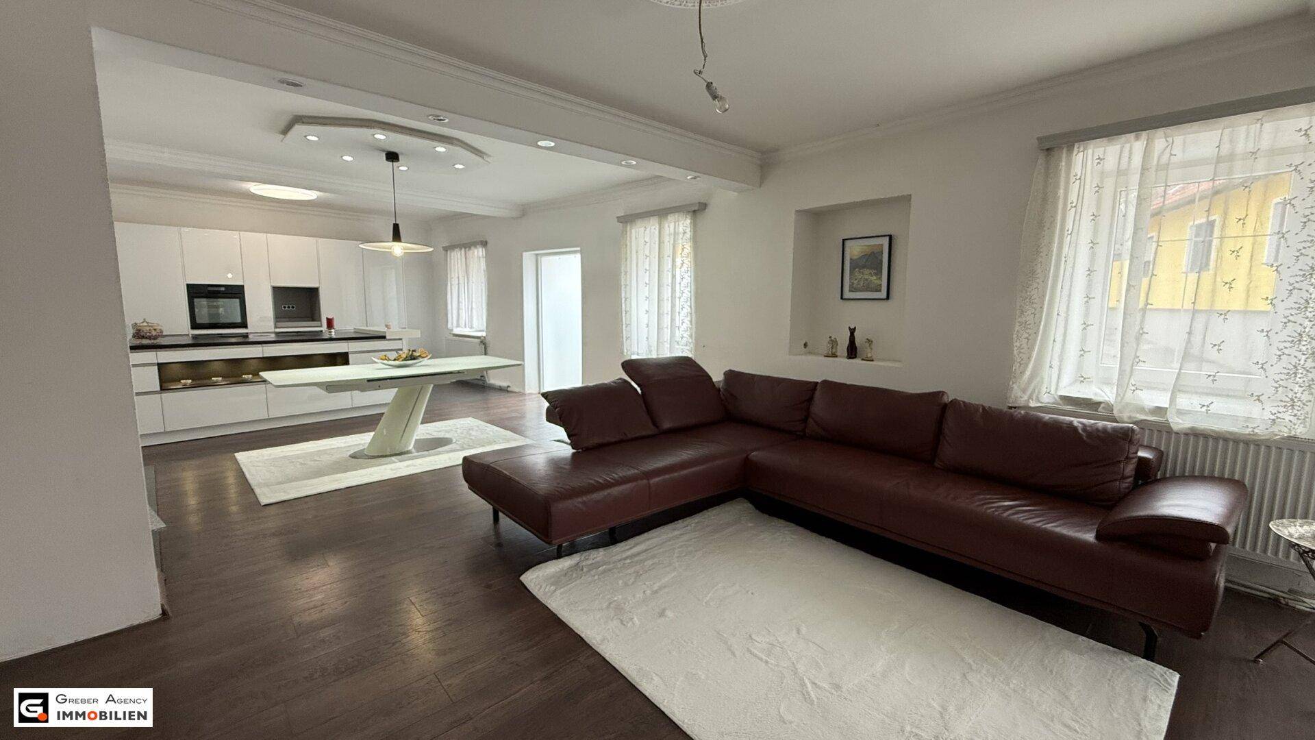 Heller Wohn-Essbereich mit Ledersofa, Holzboden und offener Verbindung zur Küche.