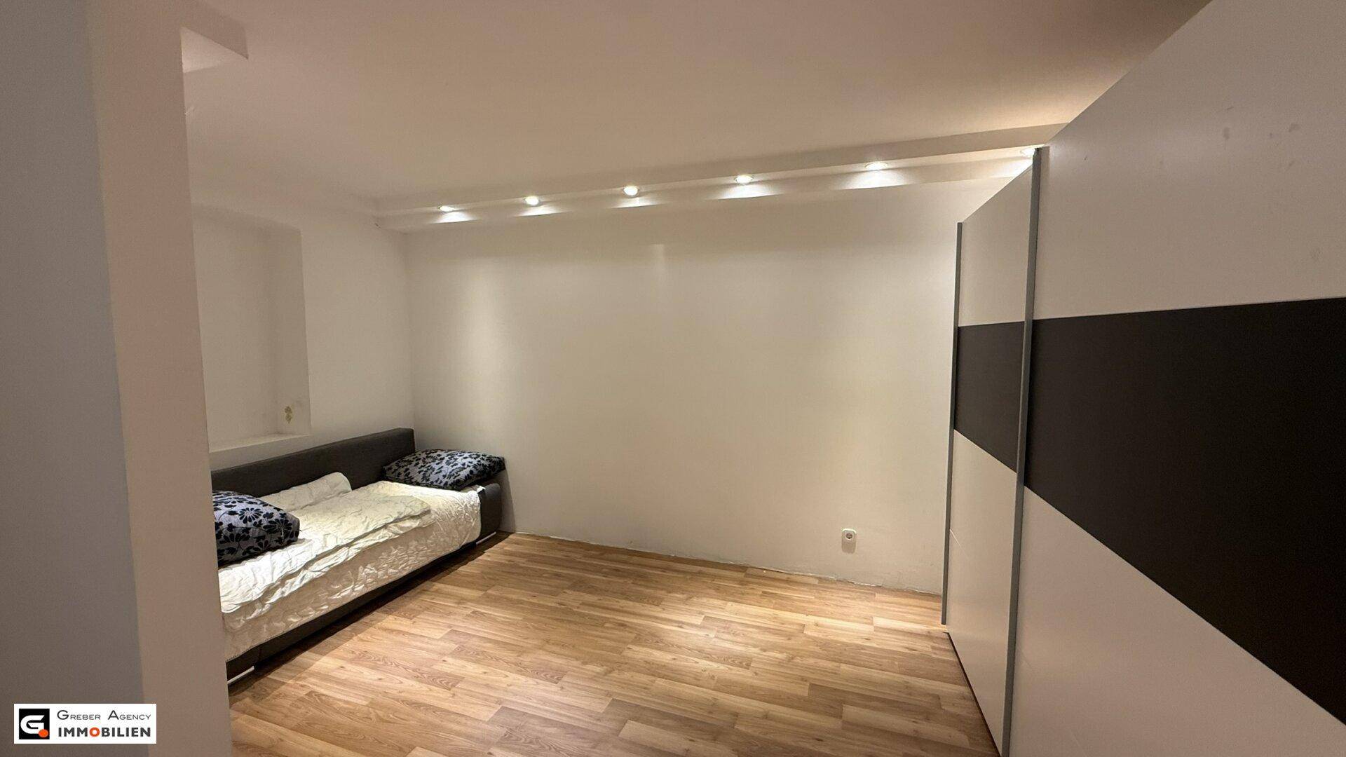 Gemütliches Schlafzimmer mit Holzboden, Schlafsofa und Einbauschrank.