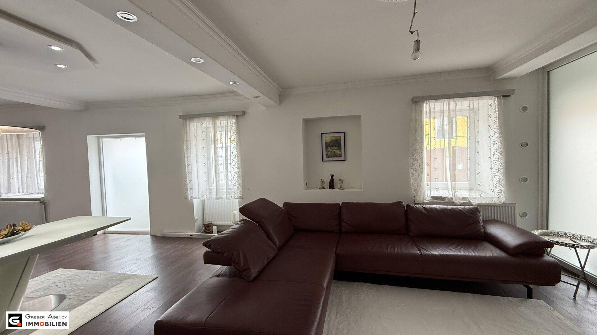 Gemütliches Wohnzimmer mit großem Ledersofa, Holzboden und viel Tageslicht.