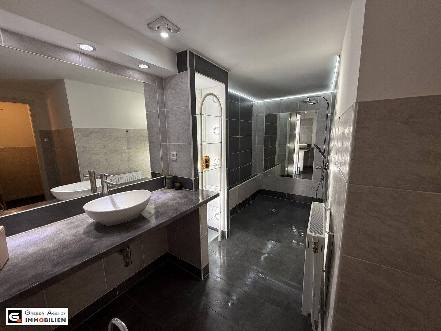 Modernes Badezimmer mit Doppelwaschbecken, großer Dusche und indirekter Beleuchtung.