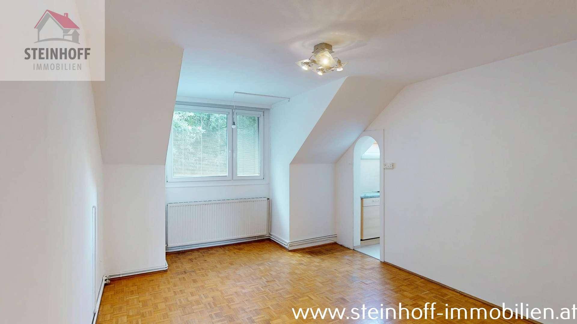 Geräumiger Raum mit Parkettboden, Fenster, Dachschrägen und einem Durchgang.