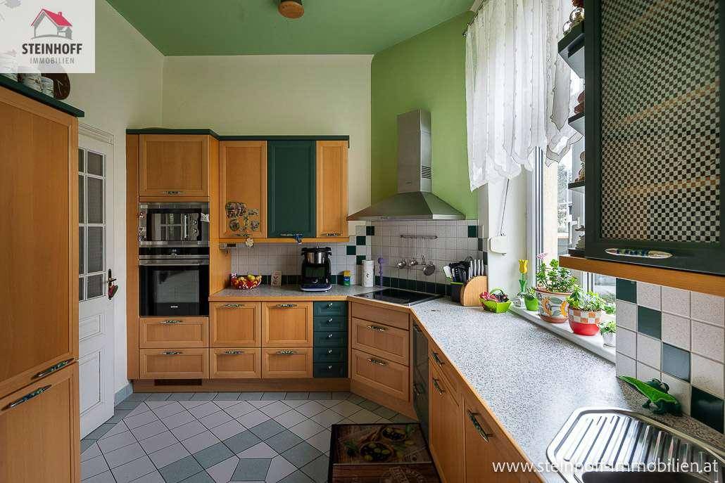 Geräumige Küche mit Holzfronten, Fliesenboden, Einbaugeräten und Blick ins Grüne.