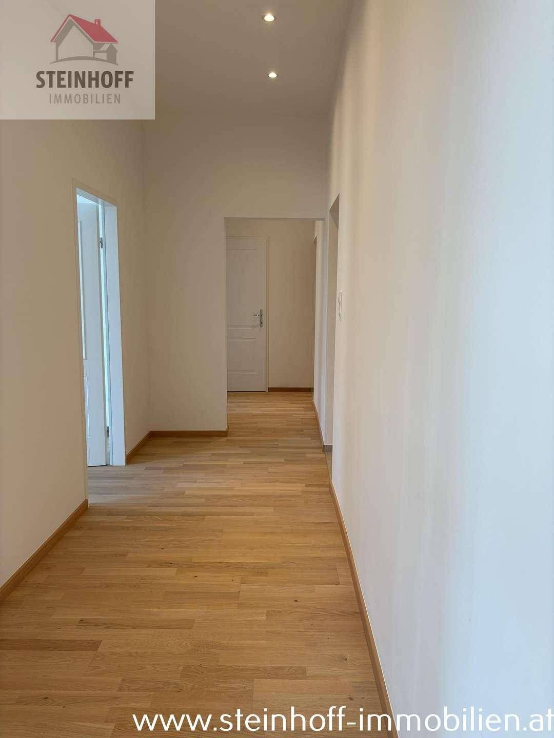 Heller Flur mit Parkettboden und integrierten Deckenstrahlern, der zu den Zimmern führt.