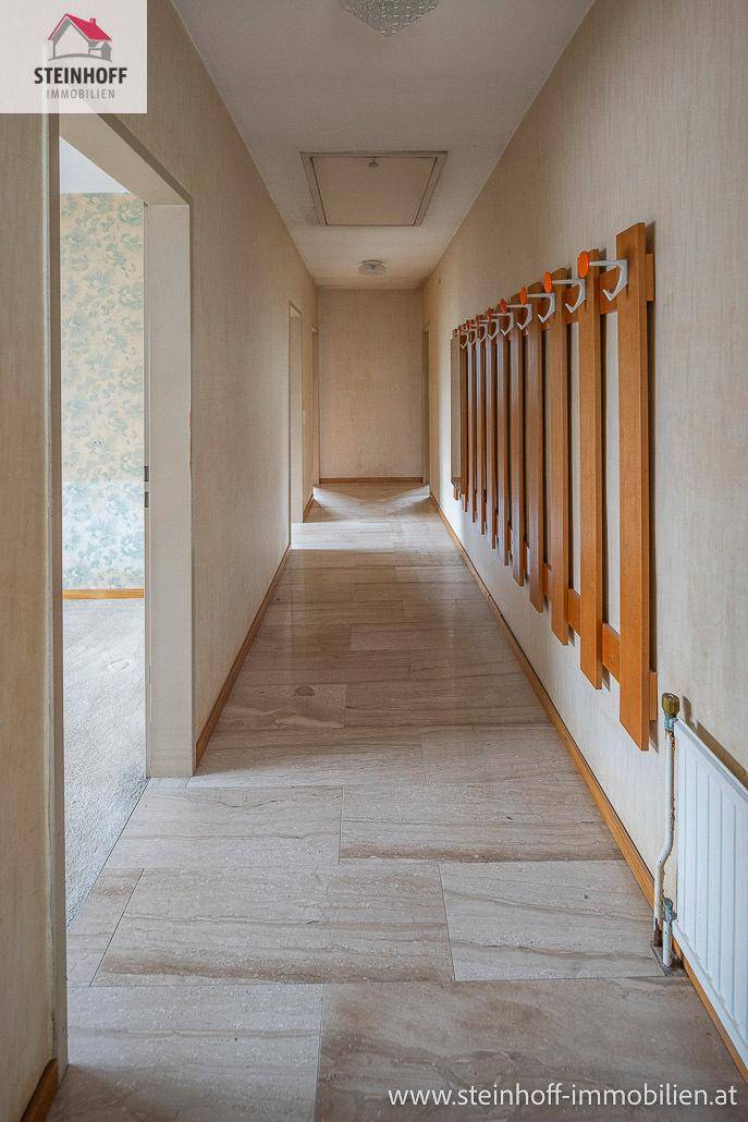 Langer Flur mit hellem Fliesenboden und Garderobe, führt zu weiteren Räumen.