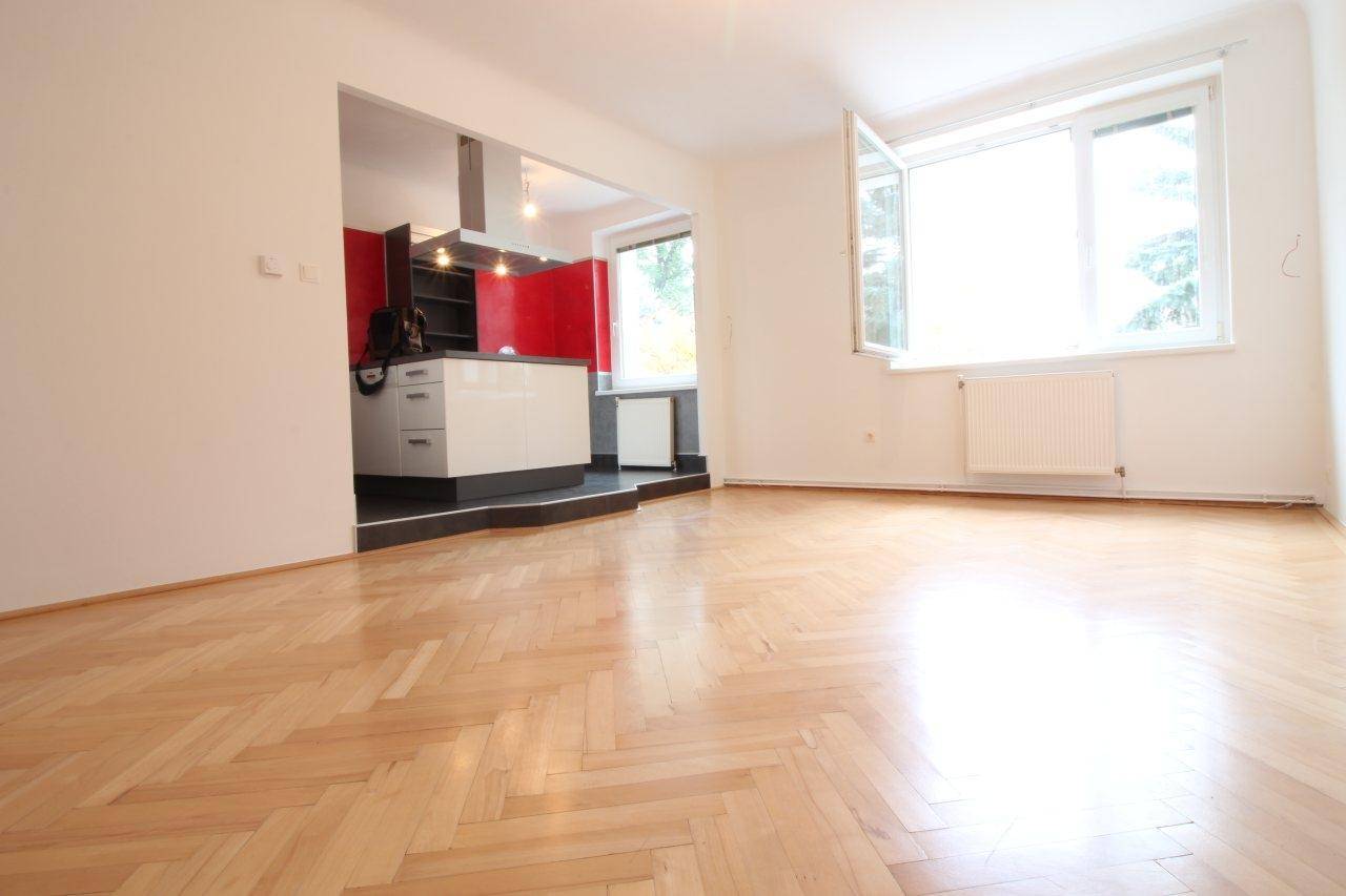 Offener Wohnbereich mit Fischgrätparkett, integrierter Küche und viel Tageslicht durch das Fenster.