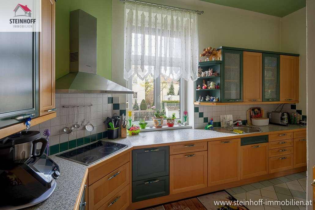 Funktionale Küche mit Holzschränken, grünen Akzenten, Einbaugeräten und Fenster.