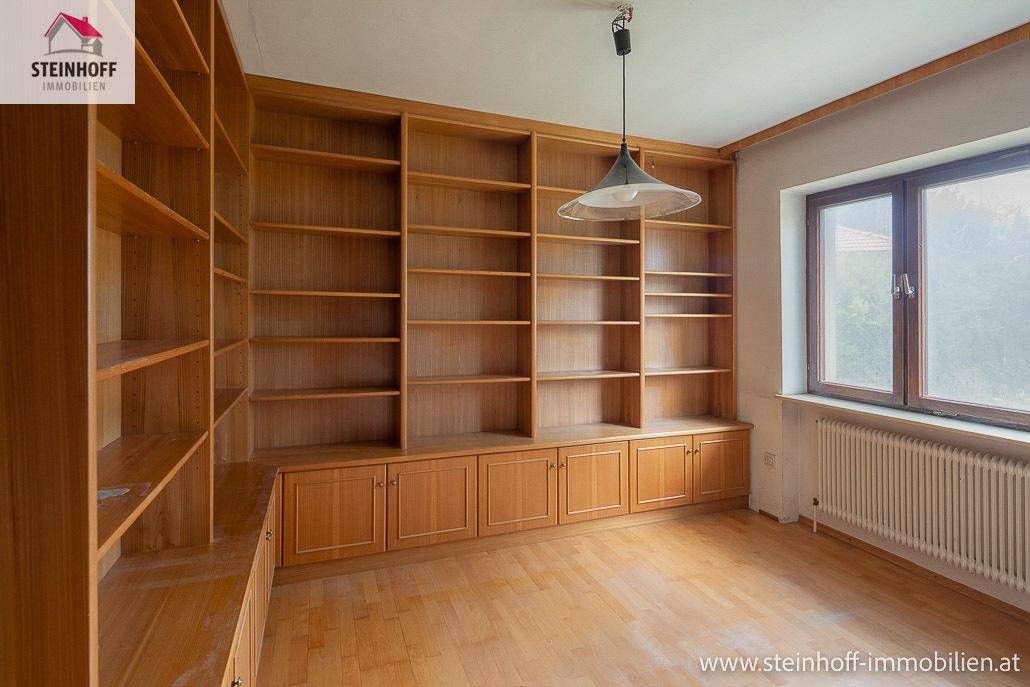 Geräumiges Zimmer mit Holzboden und großen, eingebauten Bücherregalen.