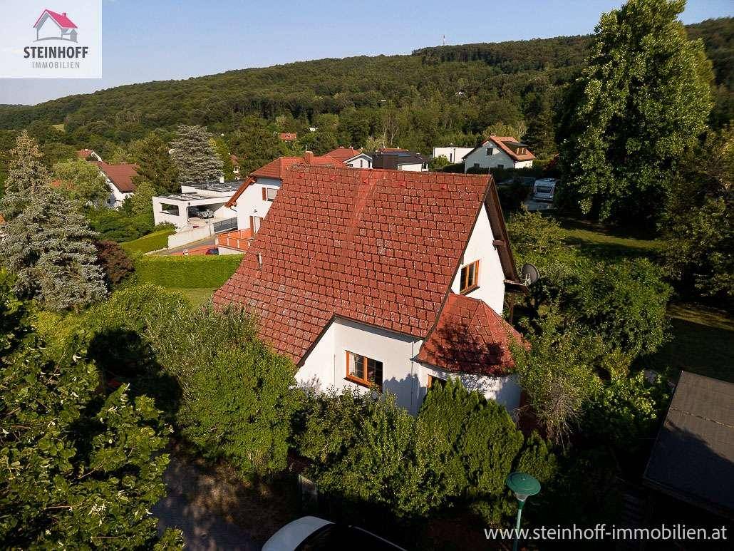 Vogelperspektive eines Einfamilienhauses mit rotem Ziegeldach, umgeben von Bäumen und Hügeln.