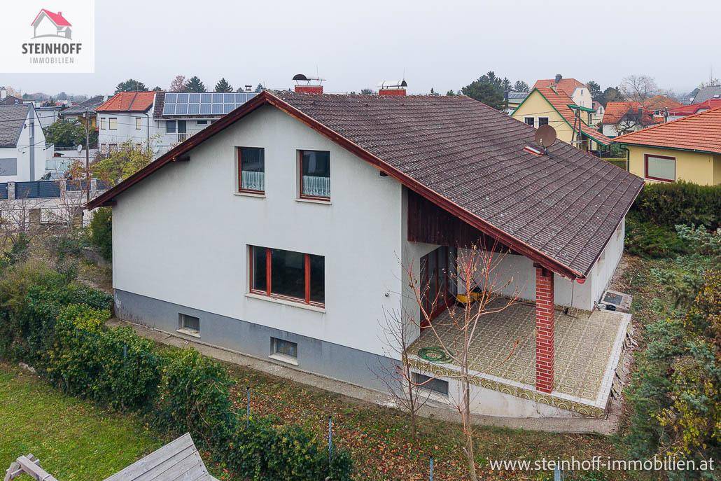 Seitenansicht des Hauses mit Terrasse, Satteldach und umliegender Vegetation.