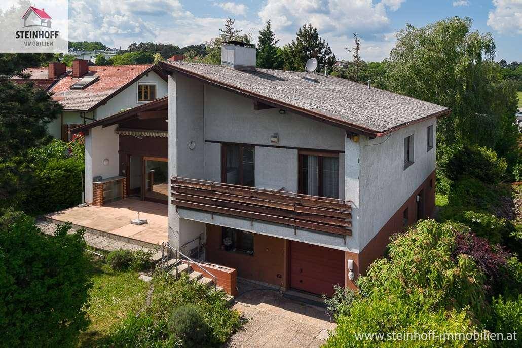 Ansicht des Hauses von hinten mit Terrasse und Balkon, umgeben von viel Grün.