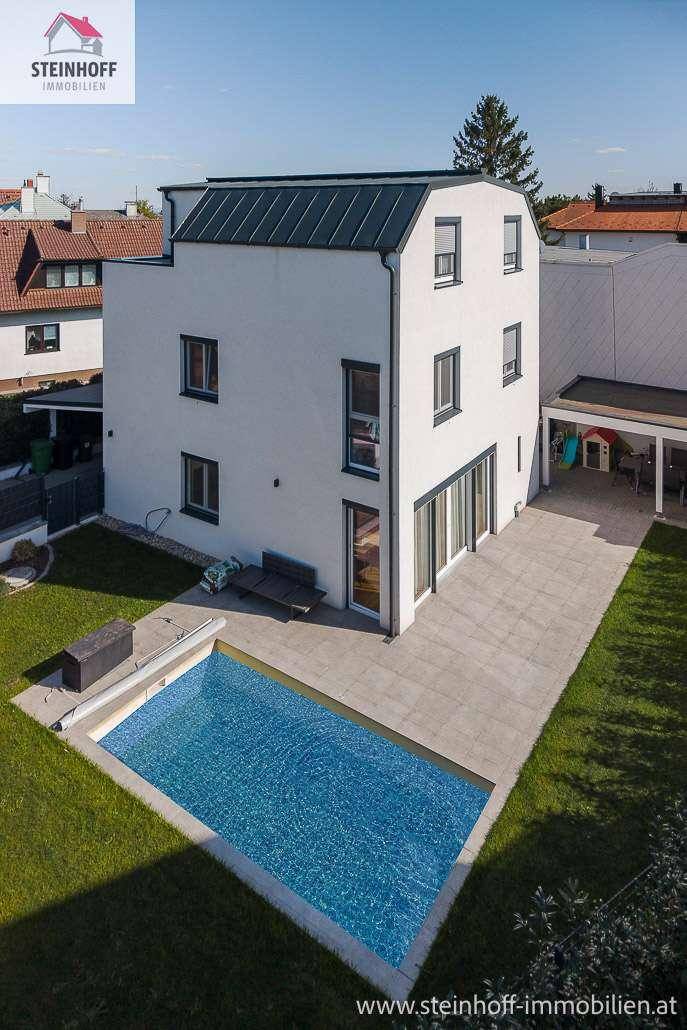 Rückansicht des modernen Hauses mit großzügigen Glasfronten, Terrasse und erfrischendem Pool.