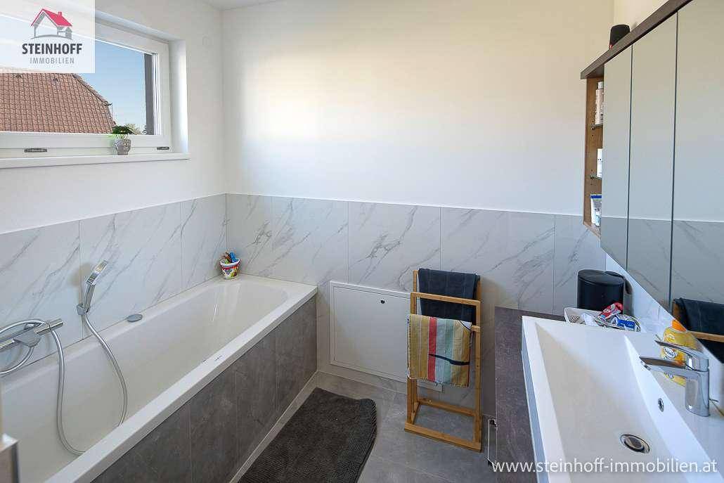 Badezimmer mit Badewanne, Einzelwaschbecken, Spiegelschrank und Fenster für natürliche Belüftung.