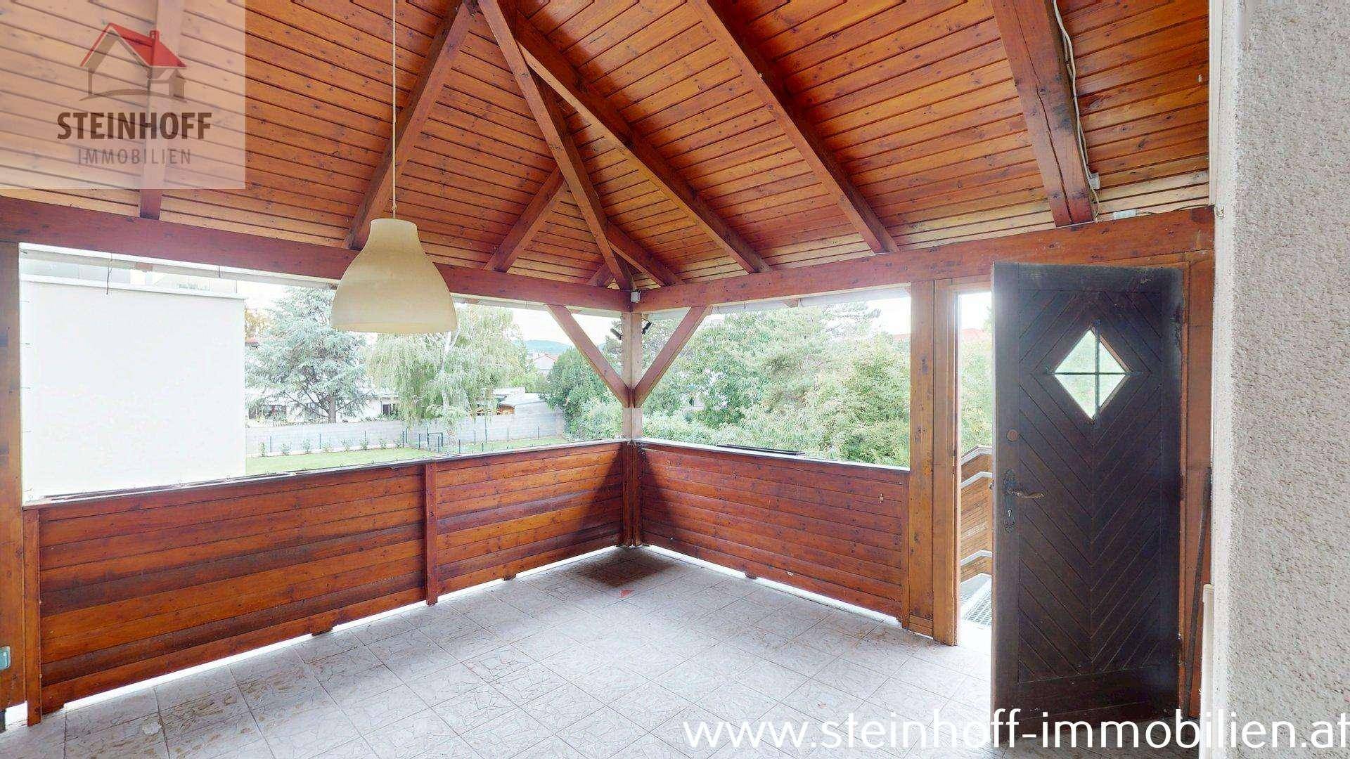 Überdachte Loggia mit Holzverkleidung und Blick ins Grüne, ideal zum Entspannen im Freien.