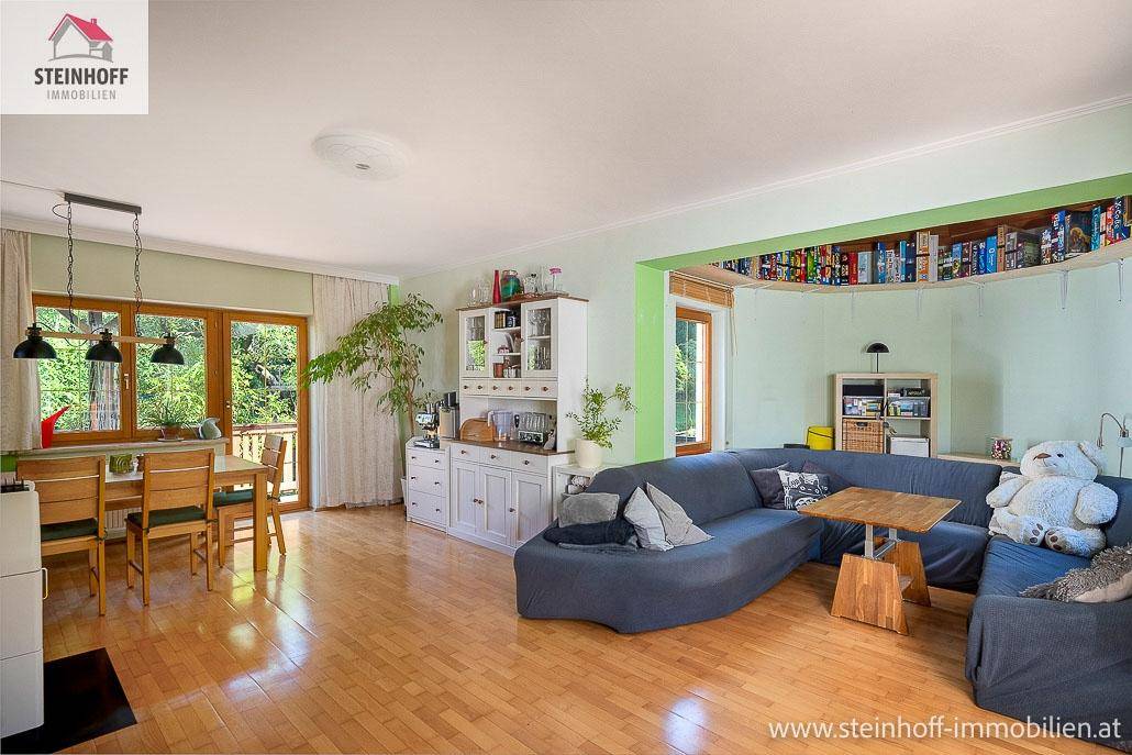 Heller Wohn- und Essbereich mit Holzboden, großem Sofa und Zugang zum Garten.